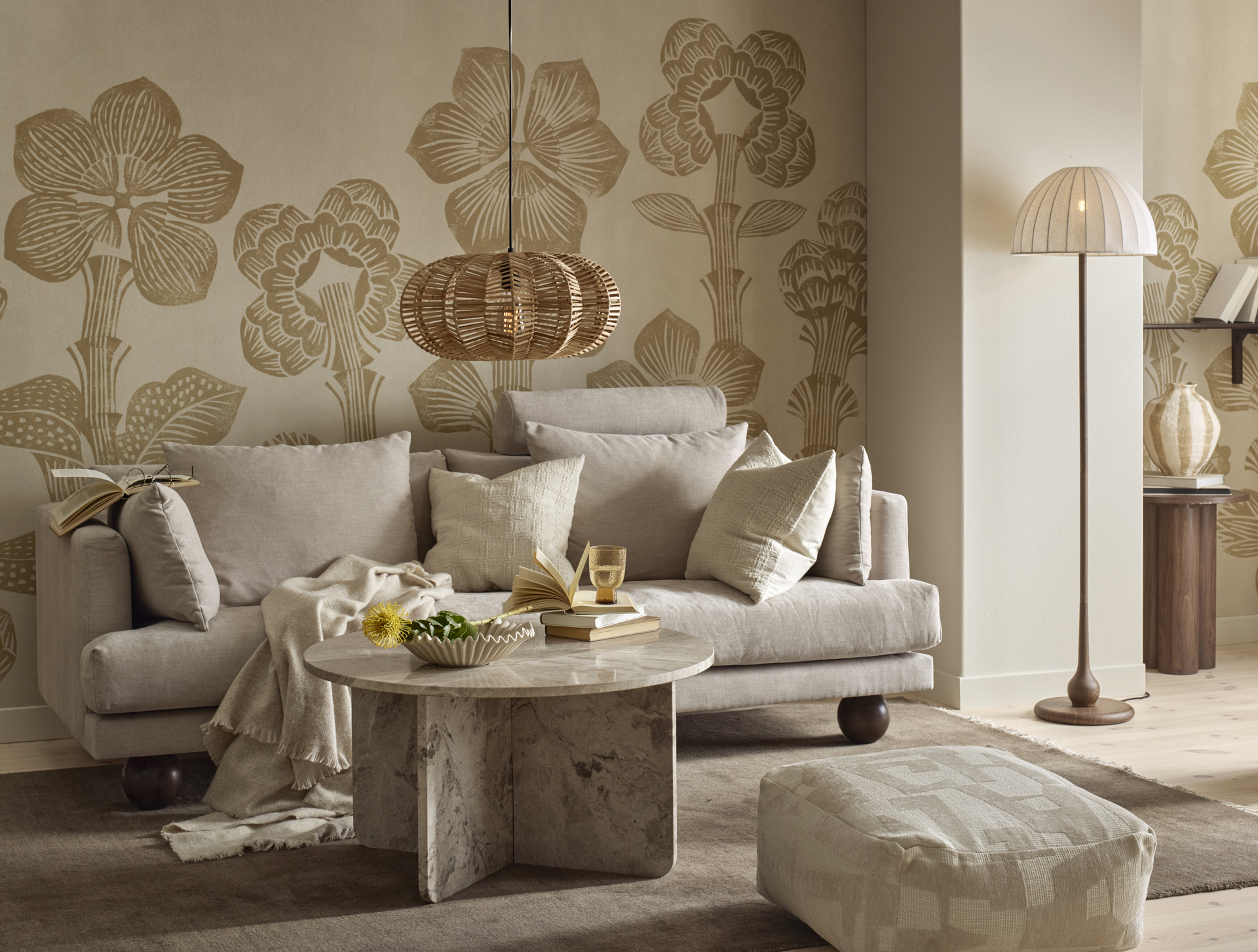 I ett vardagsrum står en beige soffa med klotformade ben bakom ett runt soffbord i beige marmor