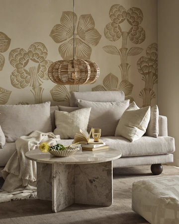 I ett vardagsrum står en beige soffa med klotformade ben bakom ett runt soffbord i beige marmor