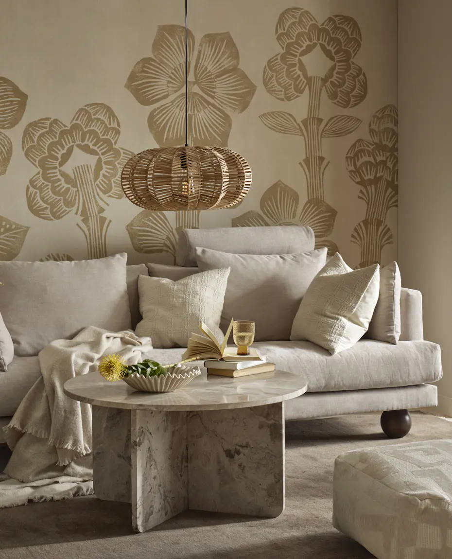 I ett vardagsrum står en beige soffa med klotformade ben bakom ett runt soffbord i beige marmor