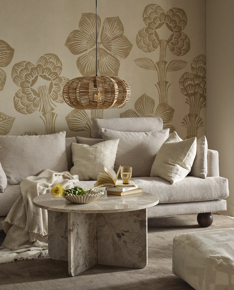 I ett vardagsrum står en beige soffa med klotformade ben bakom ett runt soffbord i beige marmor