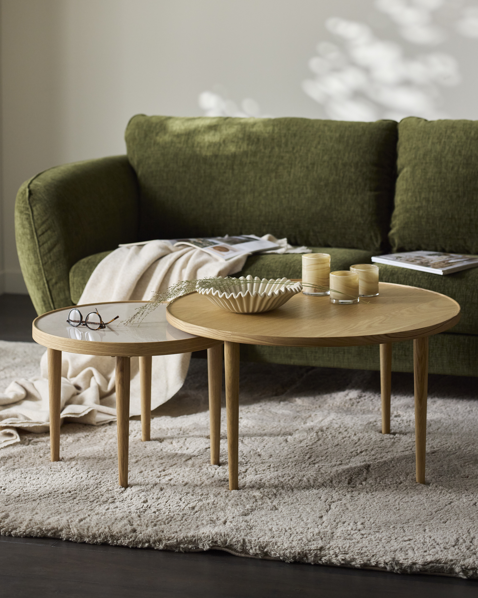 Framför en grön soffa står två runda satsbord i ek
