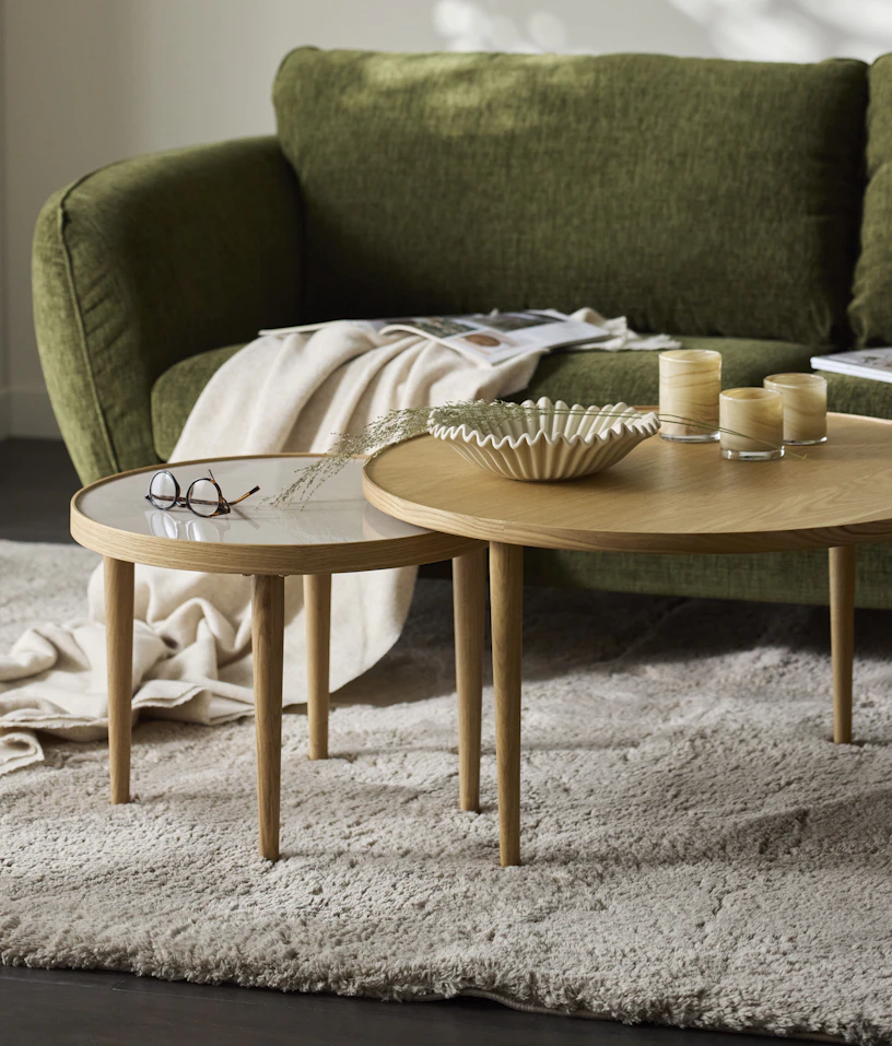 Framför en grön soffa står två runda satsbord i ek