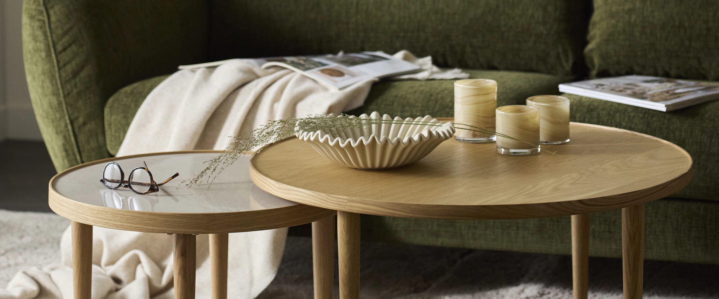 Framför en grön soffa står två runda satsbord i ek