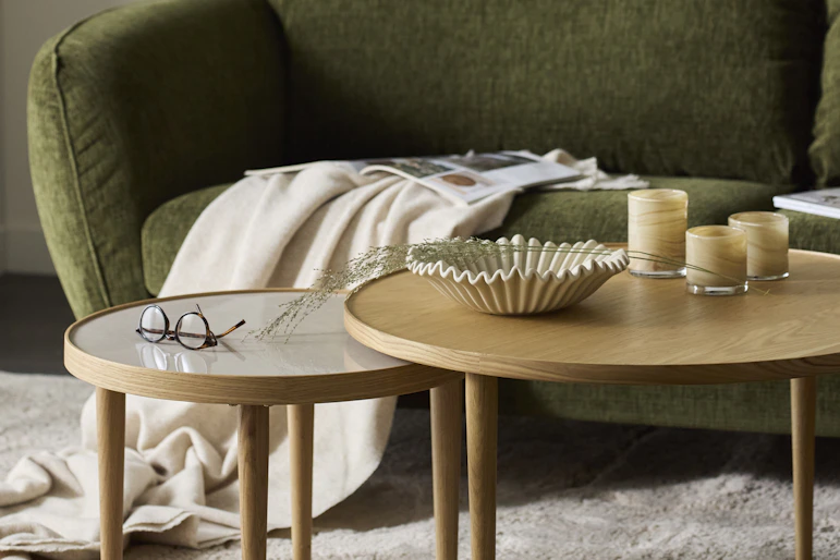 Framför en grön soffa står två runda satsbord i ek
