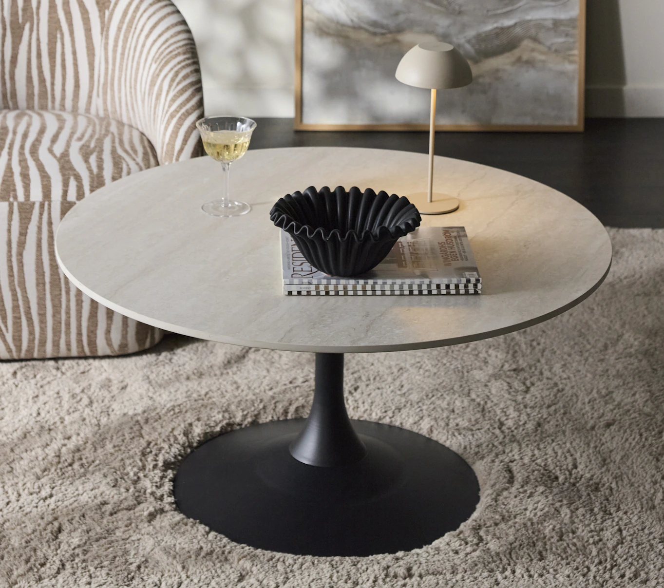 Ett soffbord med svart pelarfot och skiva i sten står på en beige matta