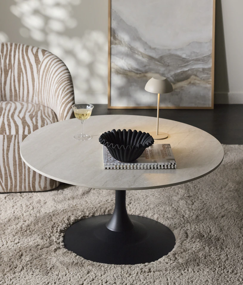 Ett soffbord med svart pelarfot och skiva i sten står på en beige matta