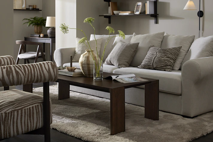 Framför en vit soffa står ett rektangulärt soffbord i mörkt trä med ribbade ben