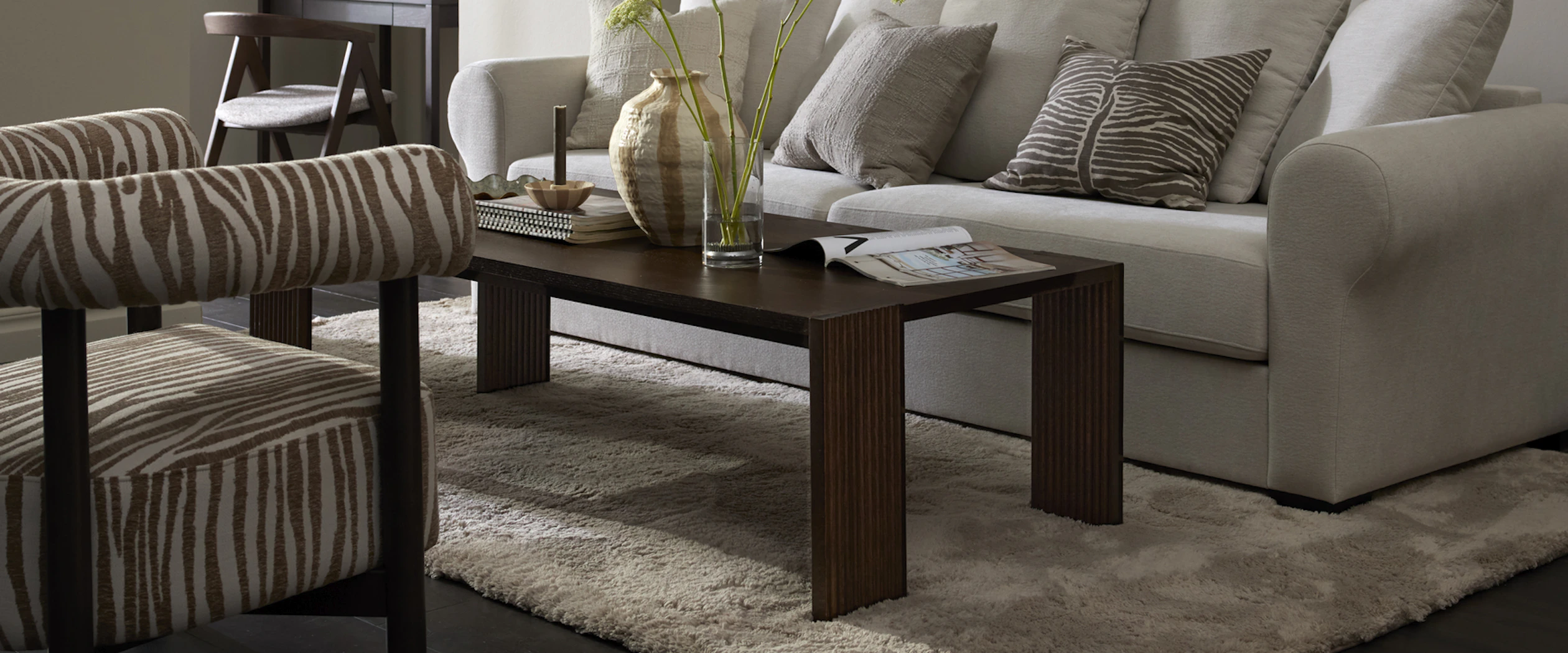 Framför en vit soffa står ett rektangulärt soffbord i mörkt trä med ribbade ben