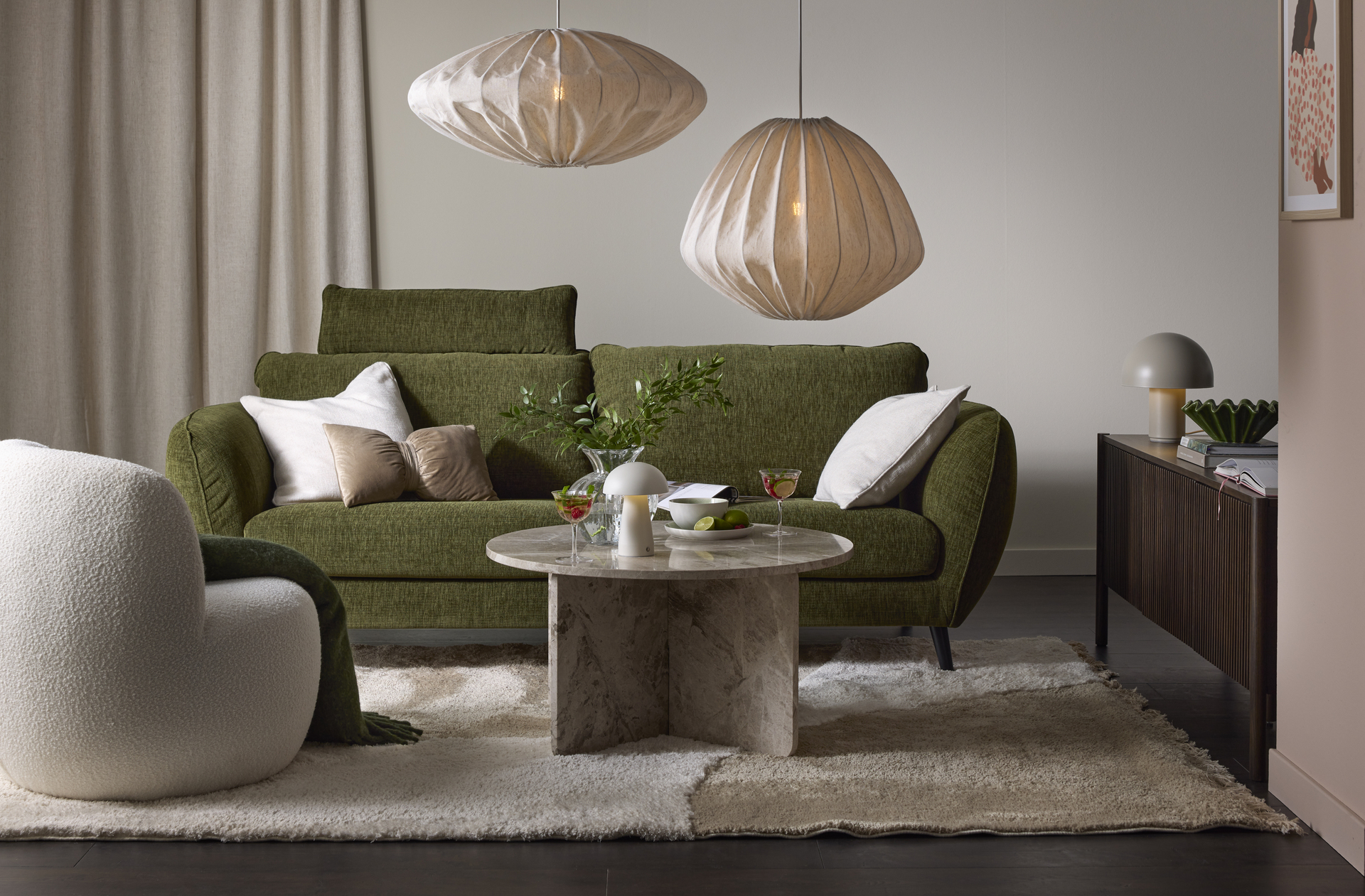 Framför en grön soffa står ett runt soffbord i marmor