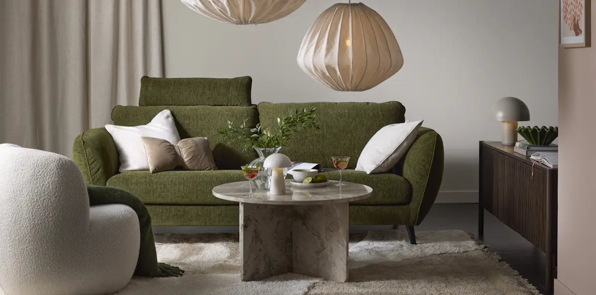 I ett beige vardagsrum står en grön soffa med bulliga armstöd bakom ett soffbord i marmor