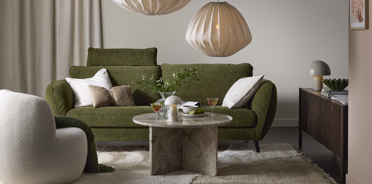 I ett beige vardagsrum står en grön soffa med bulliga armstöd bakom ett soffbord i marmor