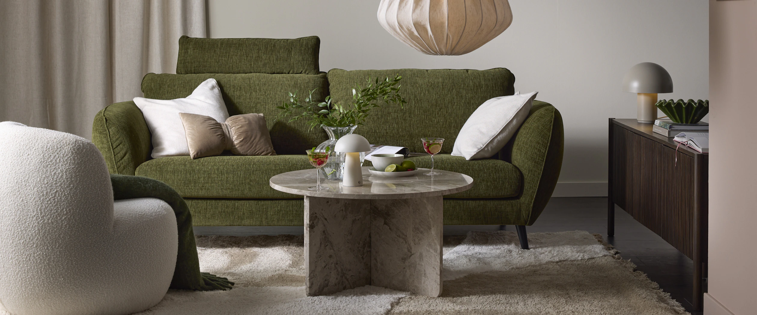 Framför en grön soffa står ett runt soffbord i marmor