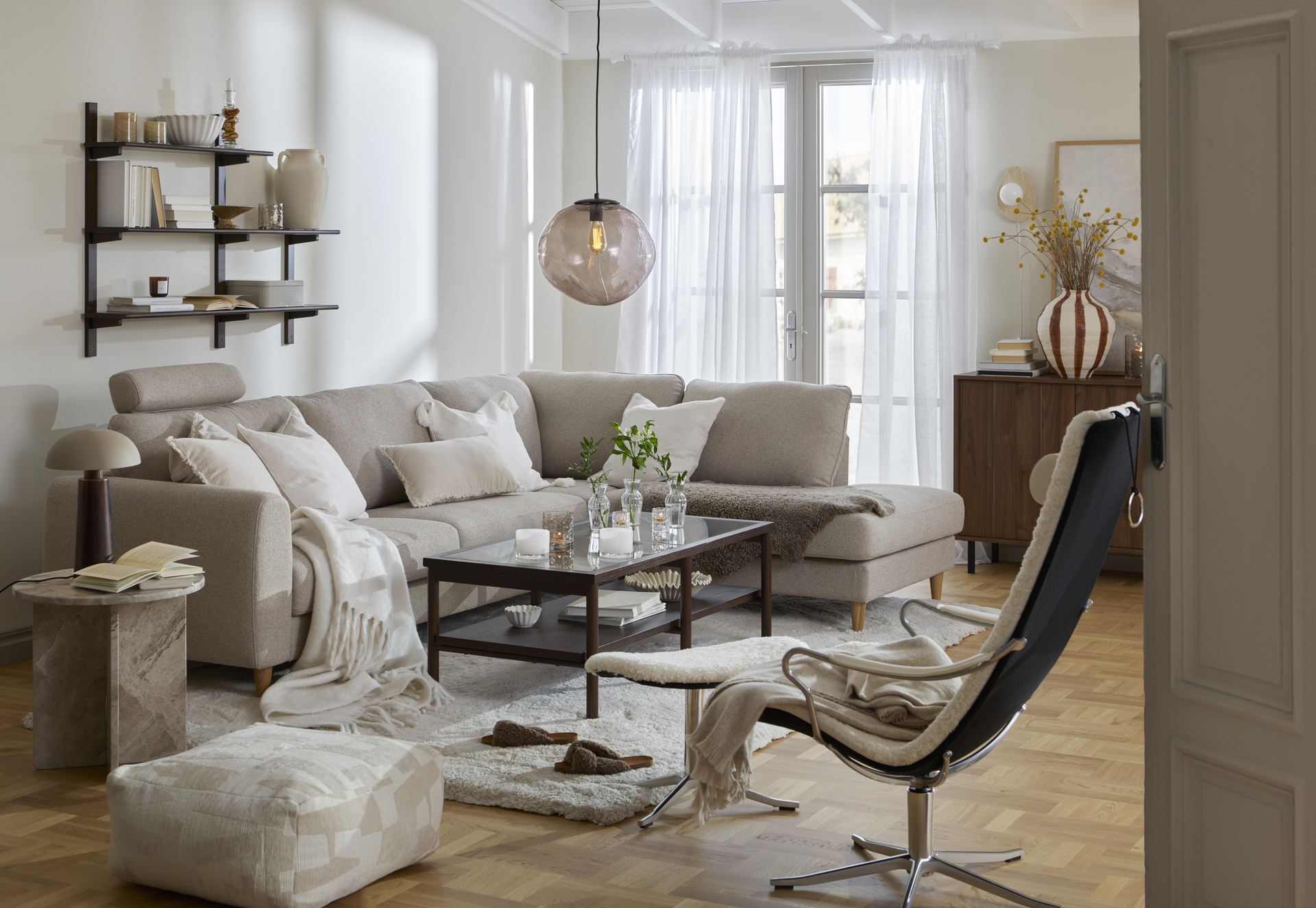 Framför en ljusgrå soffa står ett raktangulärt soffbord i trä och glas