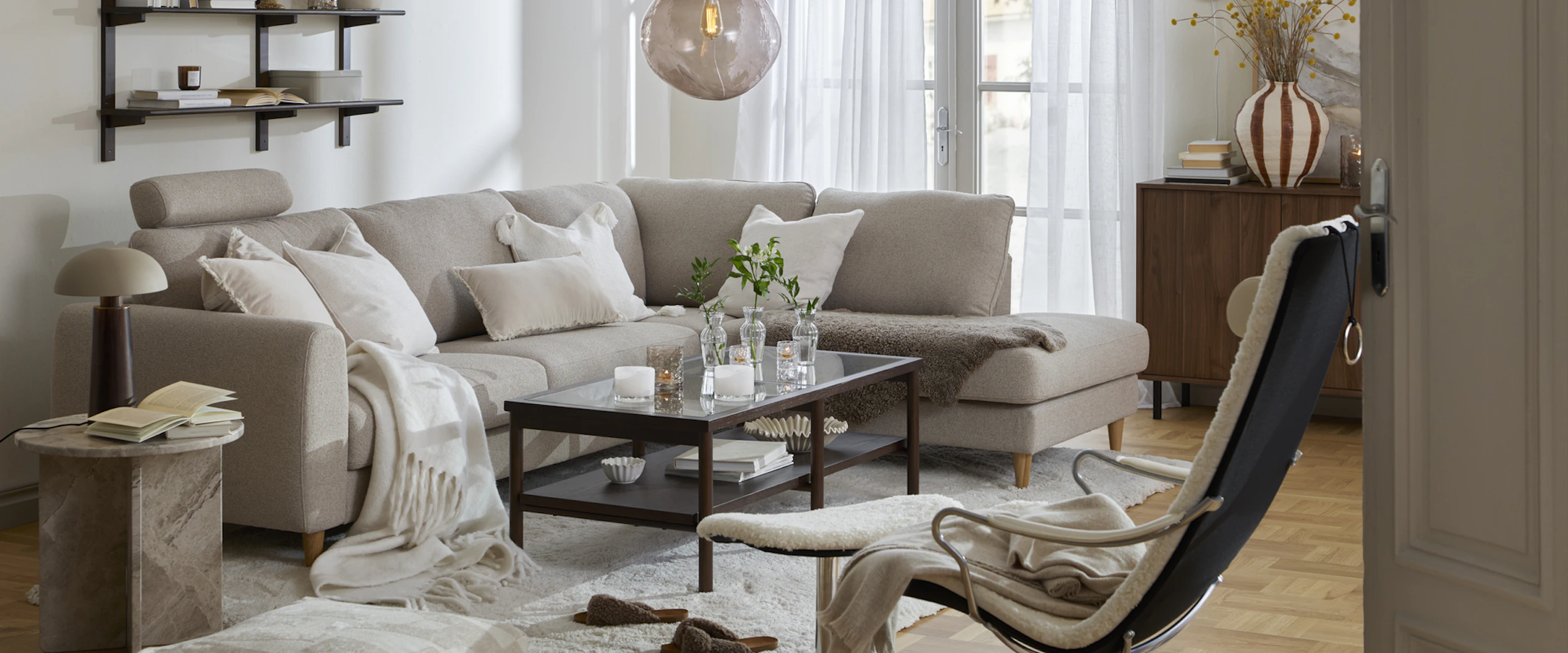 Framför en ljusgrå soffa står ett raktangulärt soffbord i trä och glas