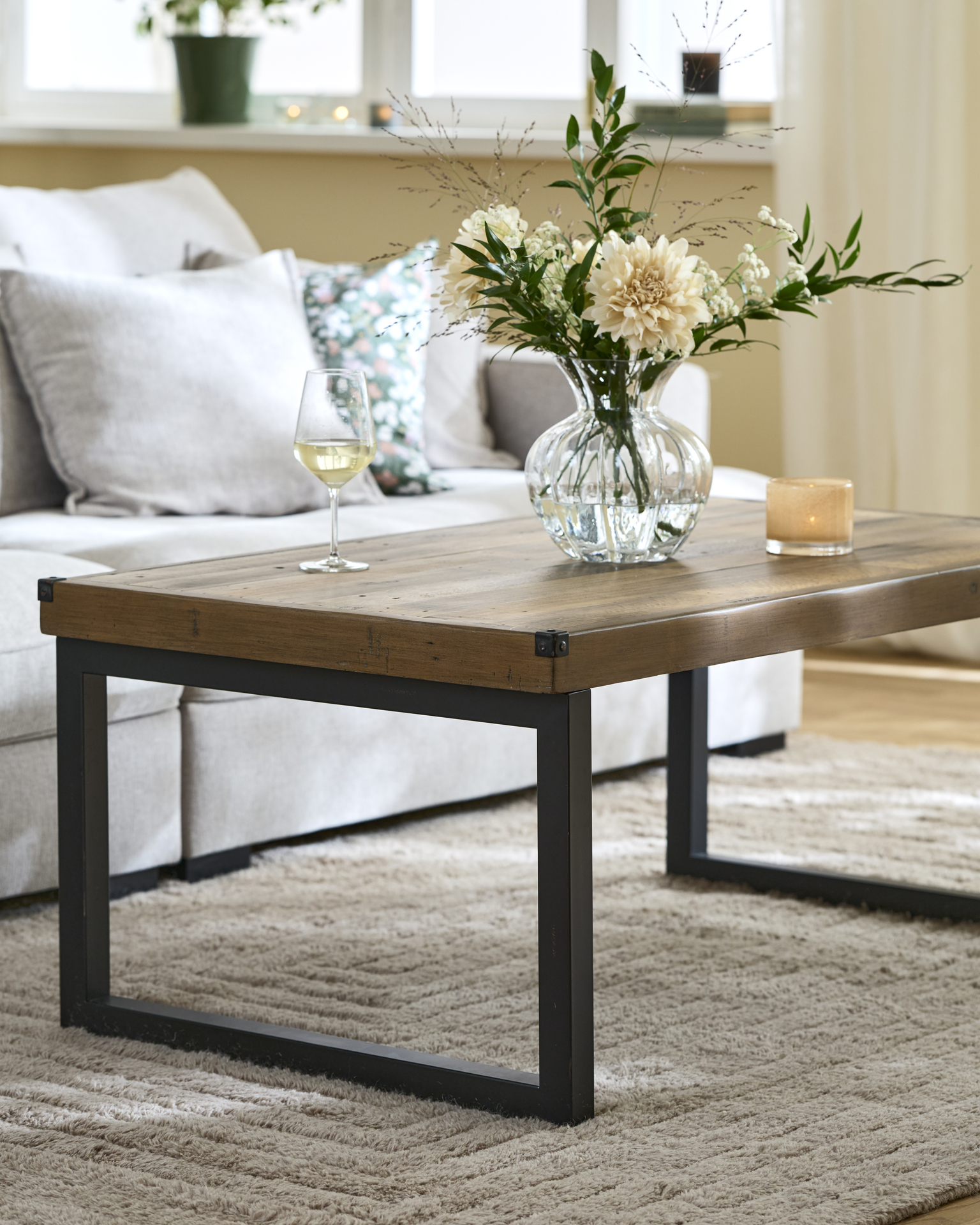 Framför en ljusgrå soffa står ett rustikt soffbord i trä med ben i metall