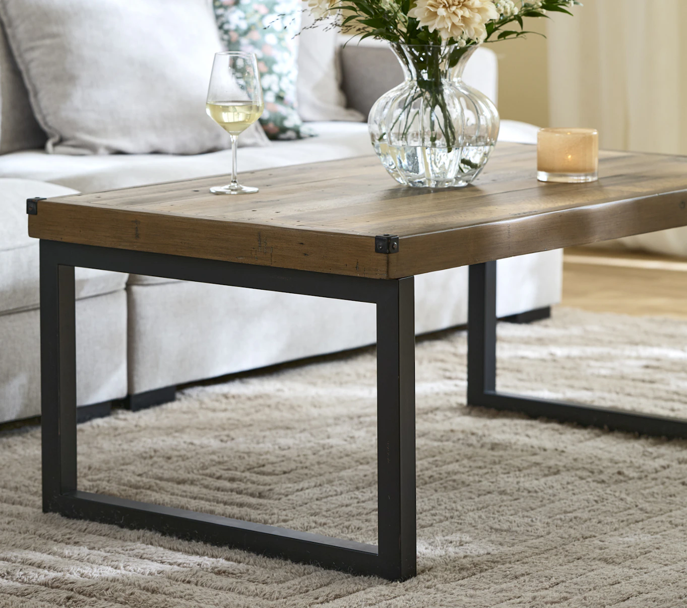 Framför en ljusgrå soffa står ett rustikt soffbord i trä med ben i metall