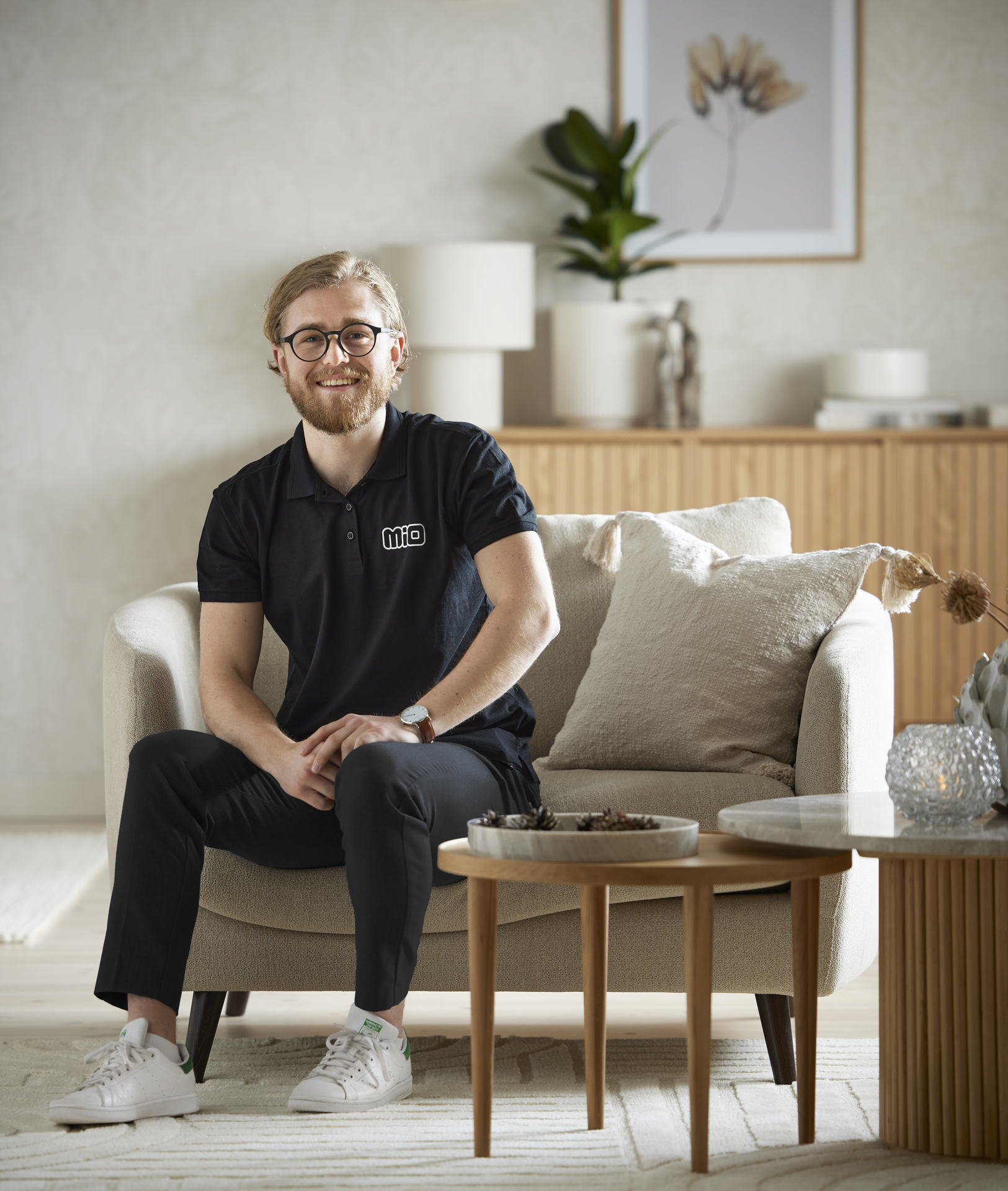 I en fåtölj sitter en man med glasögon och ler