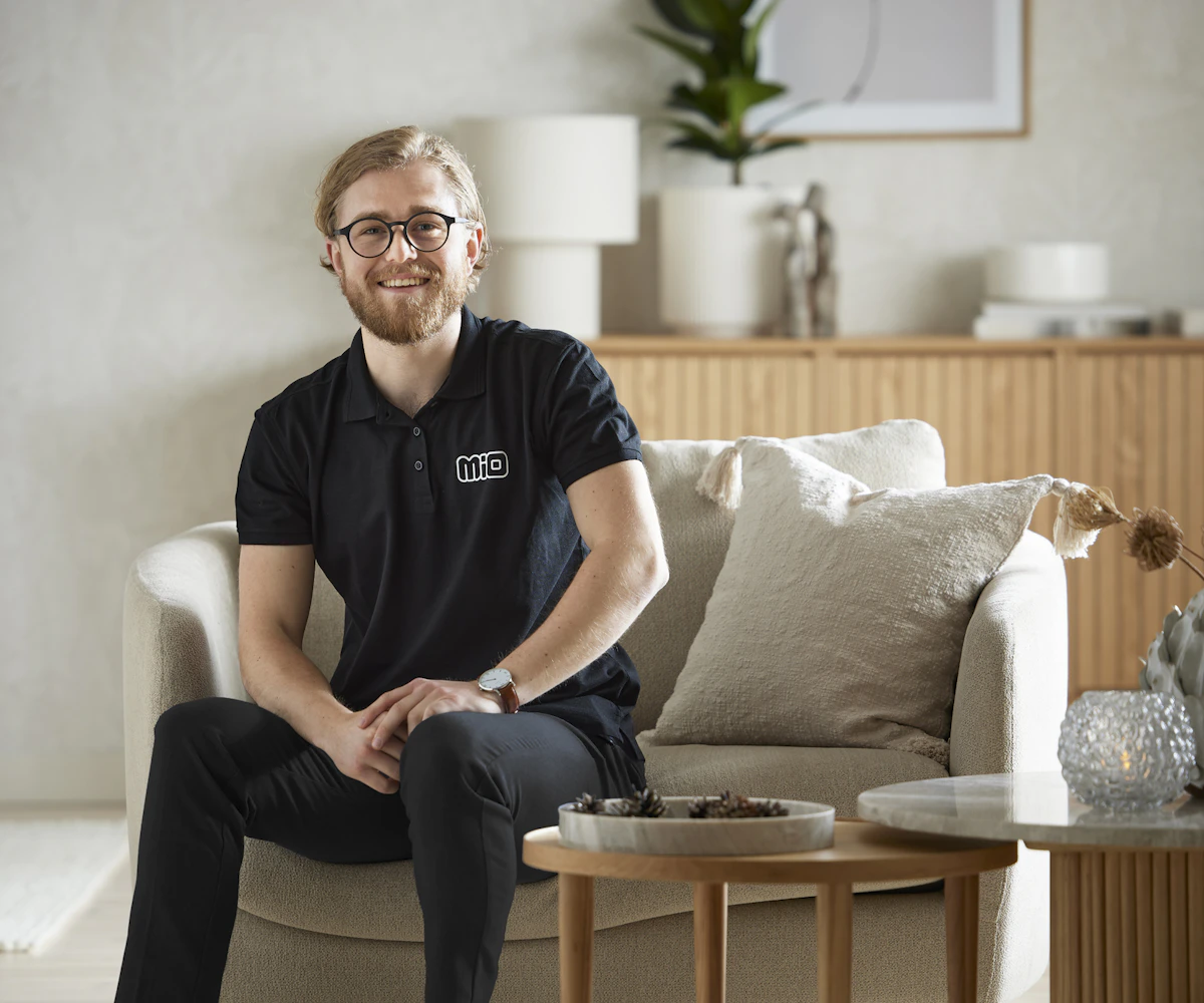 I en fåtölj sitter en man med glasögon och ler