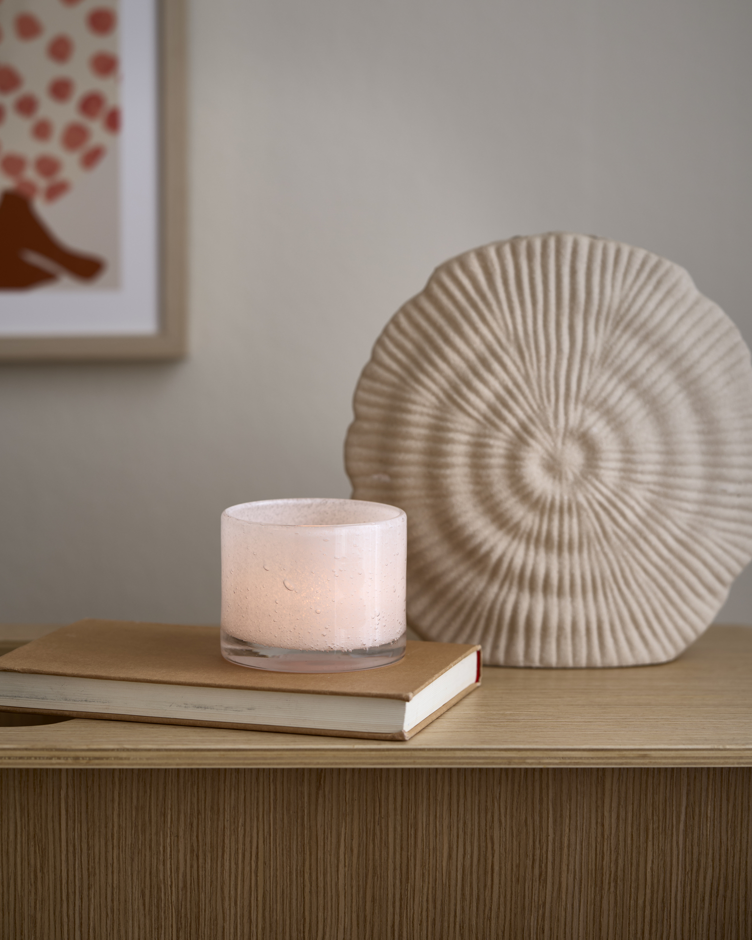 Framför en beige vas ligger en bok, på boken står en ljuslykta