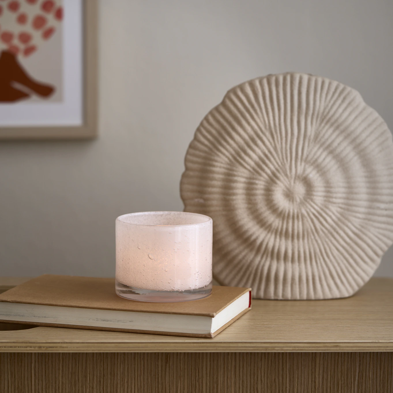 Framför en beige vas ligger en bok, på boken står en ljuslykta