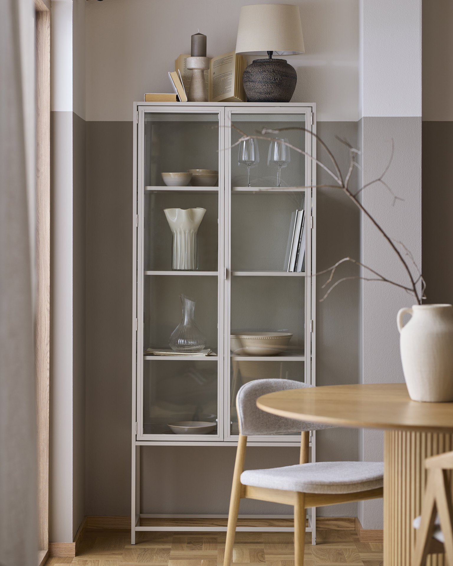 I ett beiget vitrinskåp står en mängd vackra ting i harmoniska stilleben