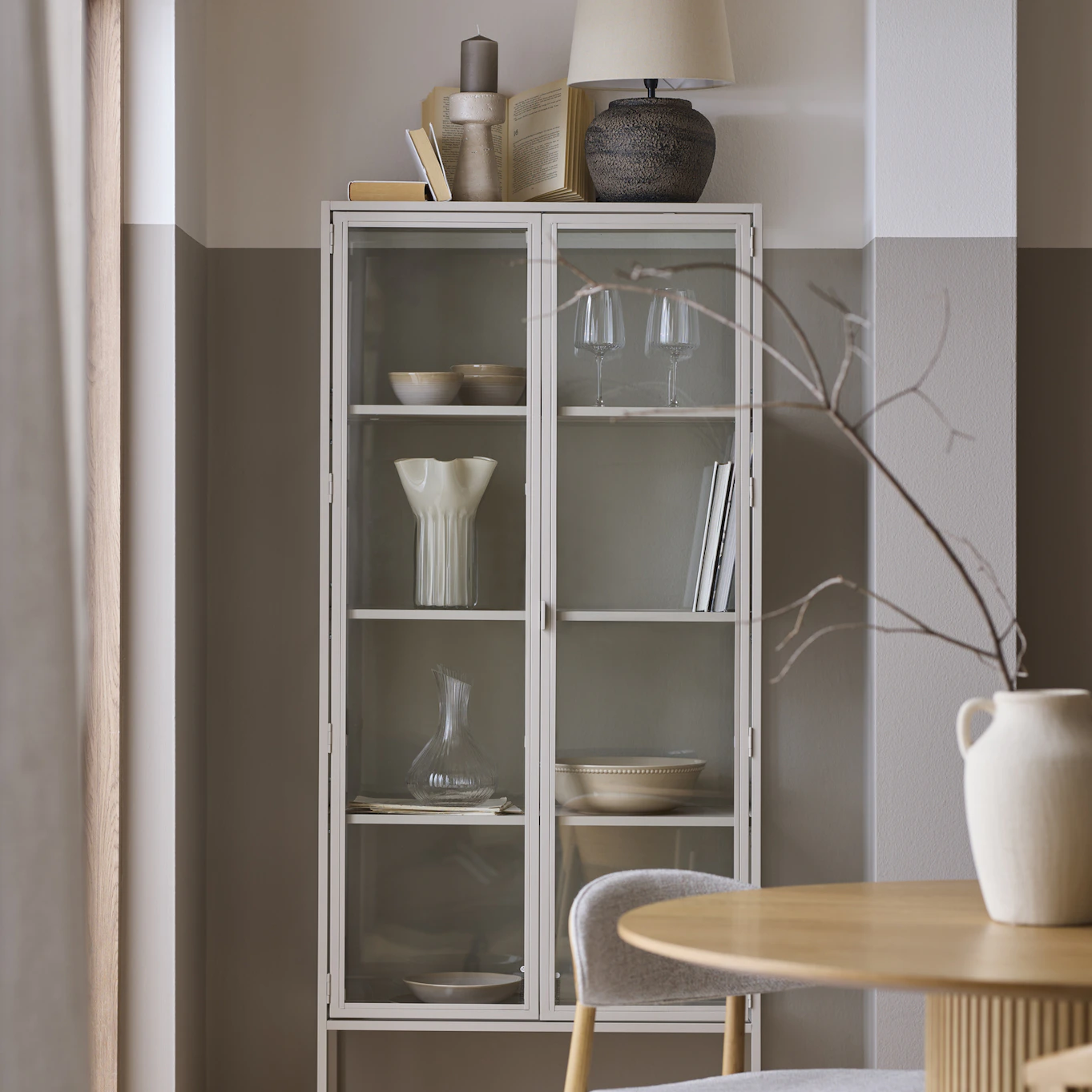 I ett beiget vitrinskåp står en mängd vackra ting i harmoniska stilleben