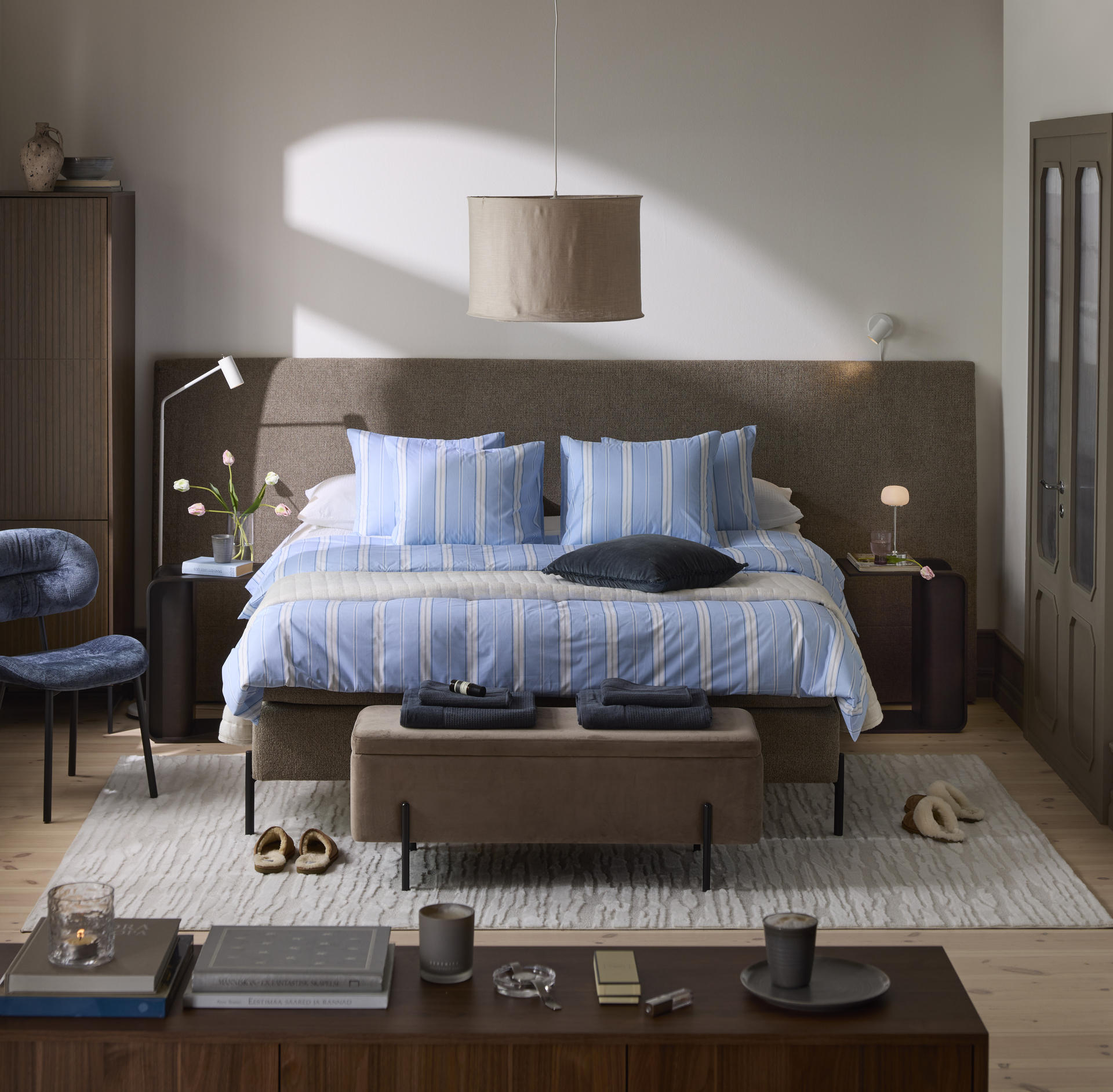 En mörkbrun säng med blårandiga sängkläder och två mörkbruna sängbord står framför en extra bred gavel.