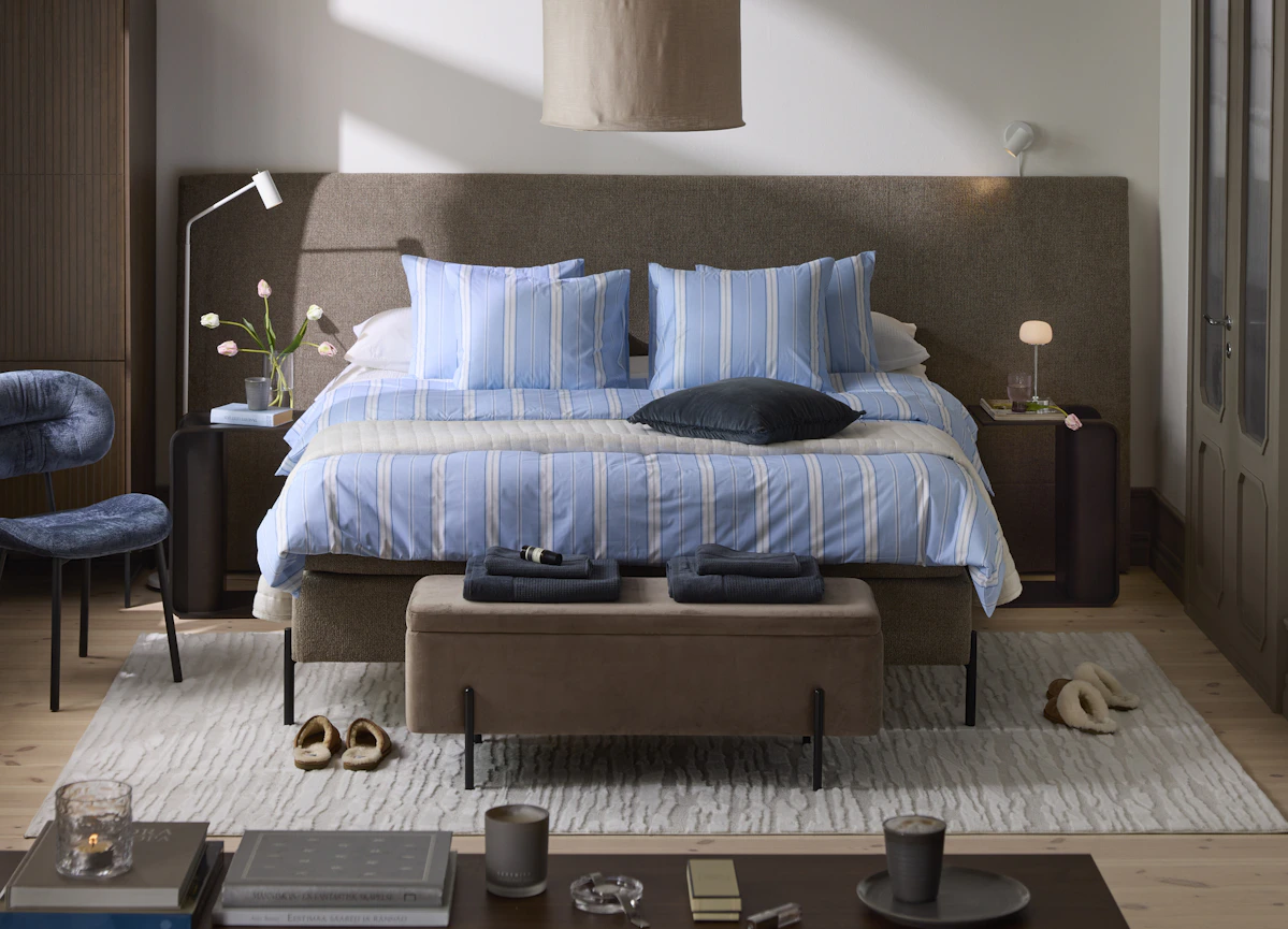 en brun kontinentalsäng med bred sänggavel står i ett sovrum. Sängen är bäddad med blå vit randiga sängkläder.