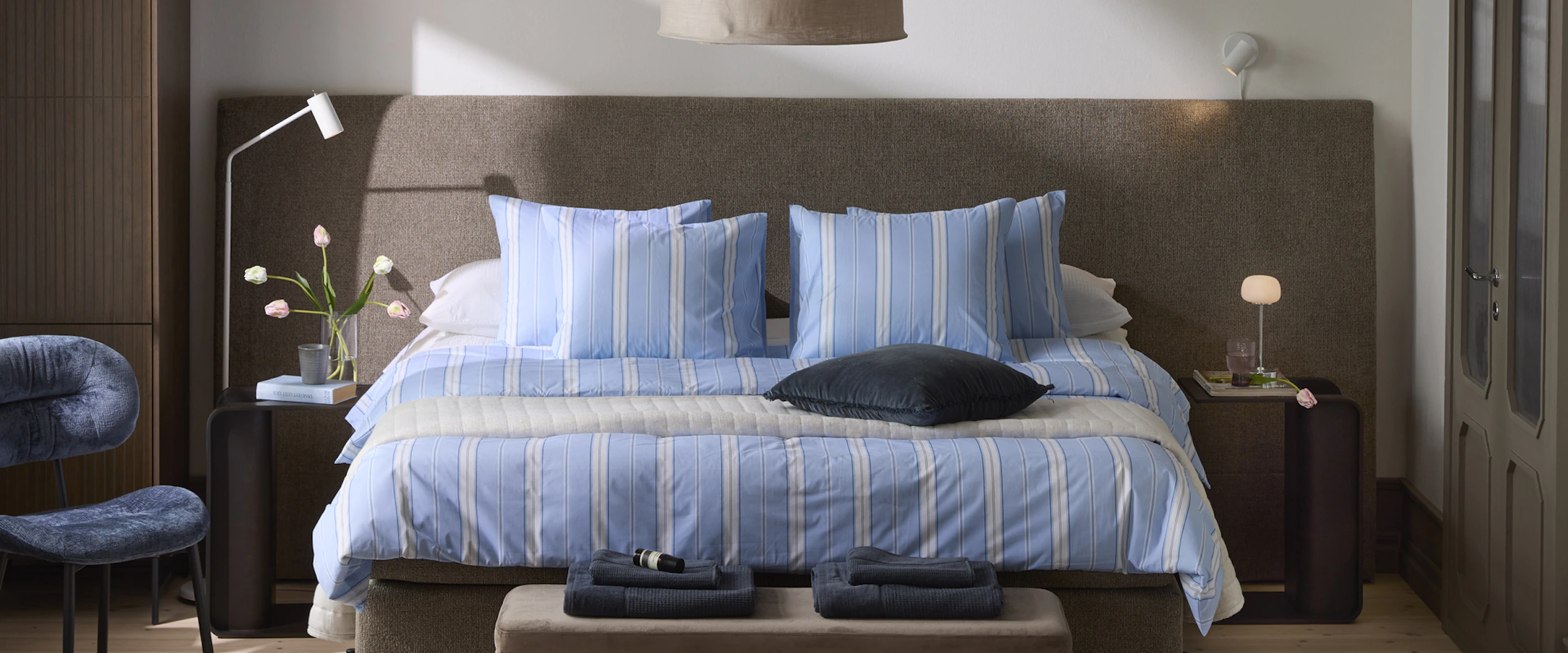 En mörkbrun säng med blårandiga sängkläder och två mörkbruna sängbord står framför en extra bred gavel.