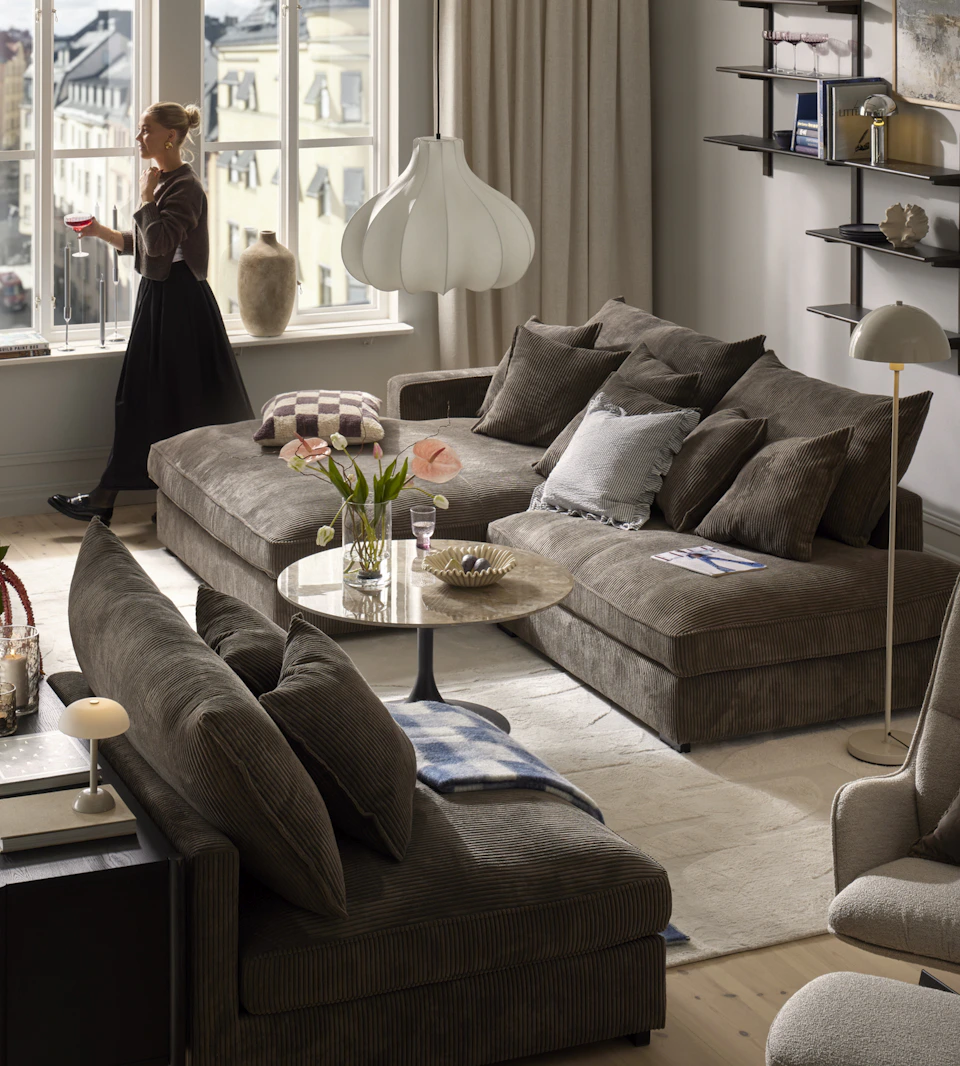 En modulsoffa i brunt manchestertyg står i ett vardagsrum som går i grått och beige med inslag av textilier i blått.