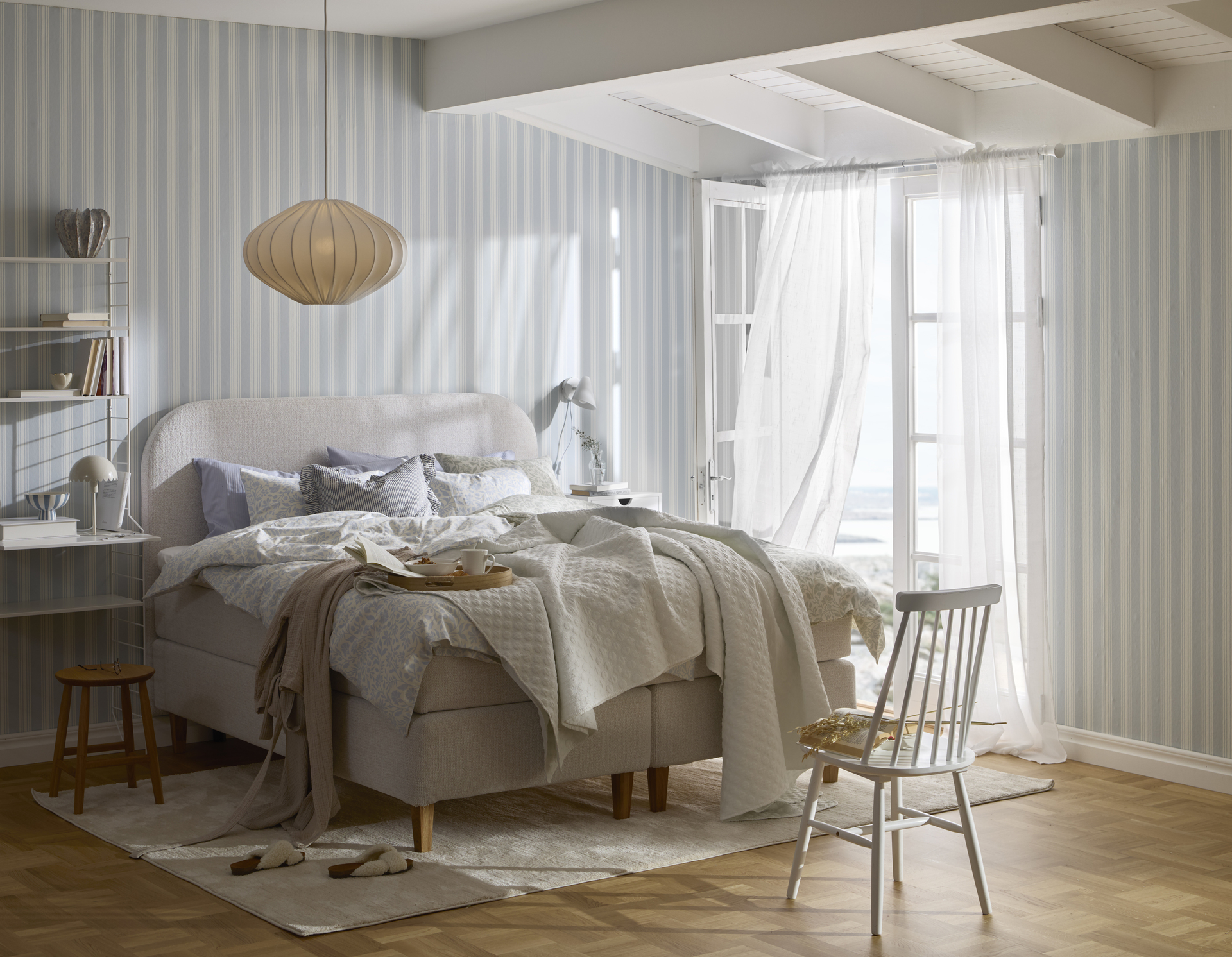 en beige säng står bäddad i ett sovrum med randiga tapeter och altandörr öppen