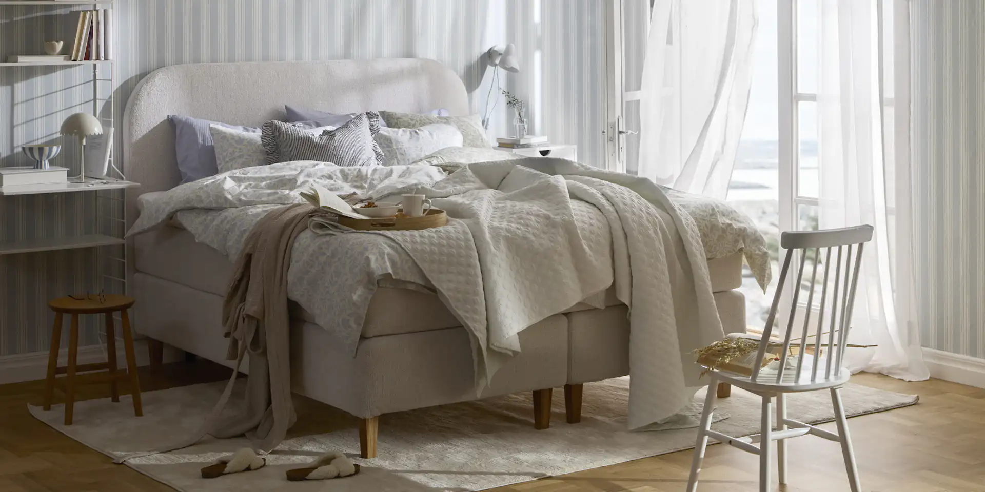 en beige säng står bäddad i ett sovrum med randiga tapeter och altandörr öppen