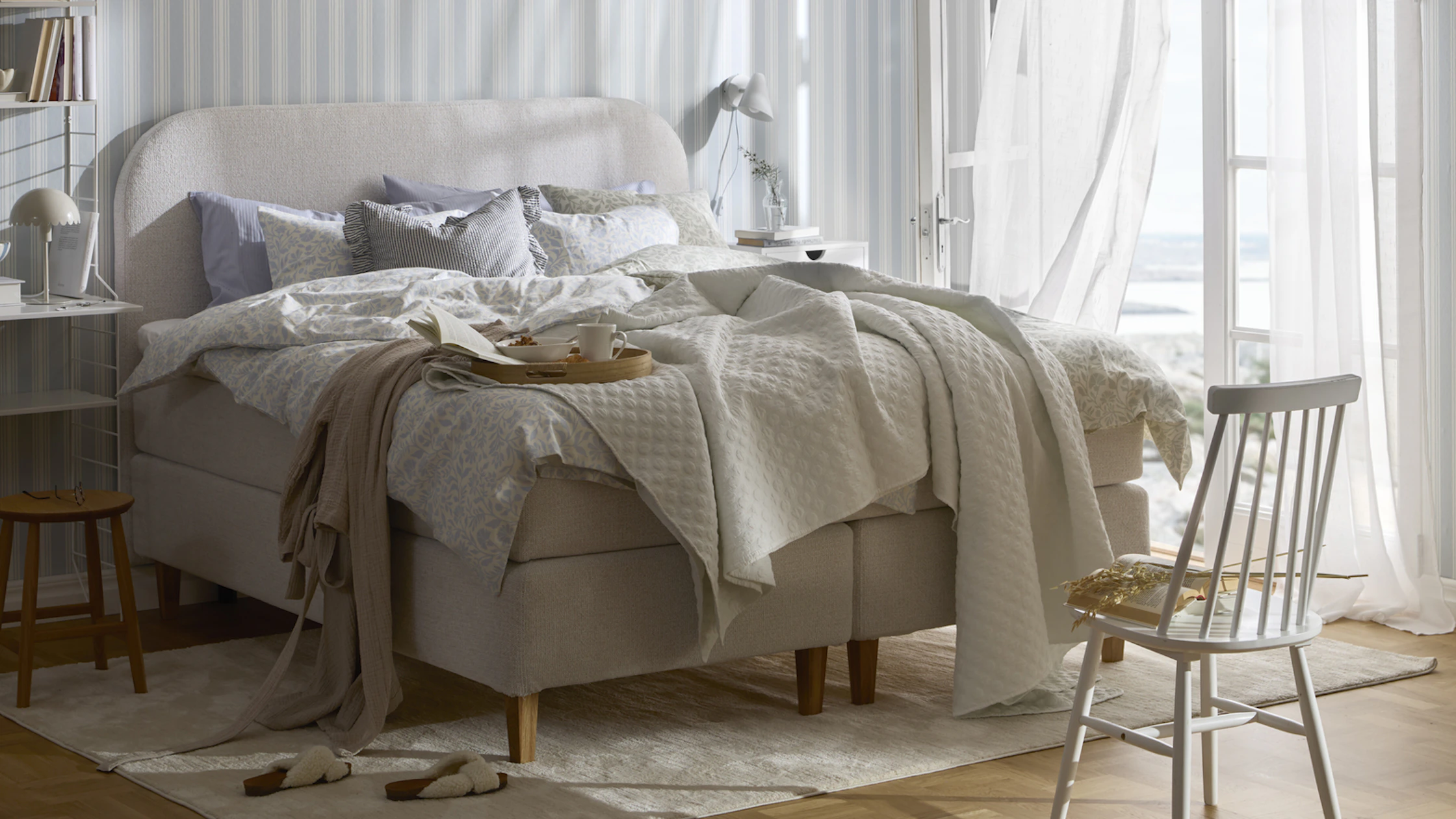 en beige säng står bäddad i ett sovrum med randiga tapeter och altandörr öppen