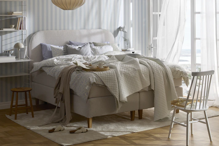 en beige säng står bäddad i ett sovrum med randiga tapeter och altandörr öppen