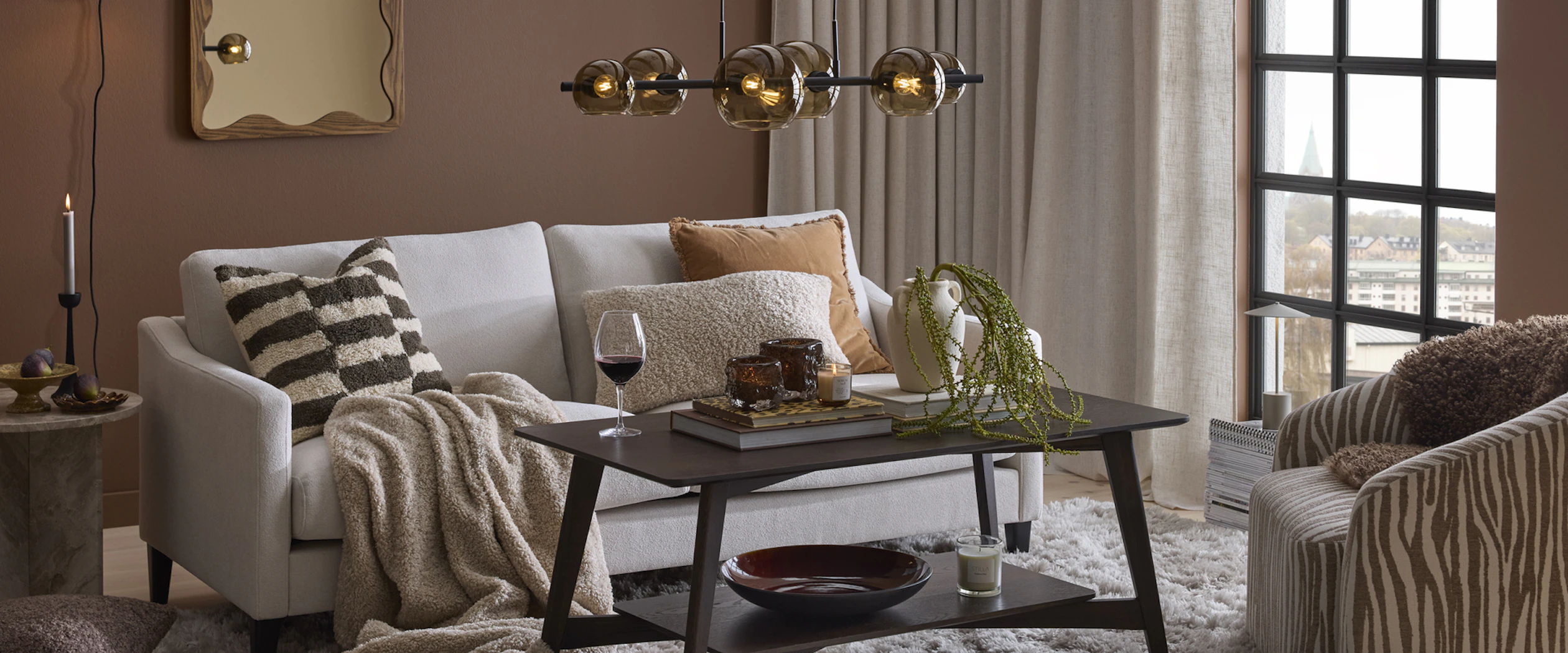 I ett brunt vardagsrum står en soffa framför beiga gardiner