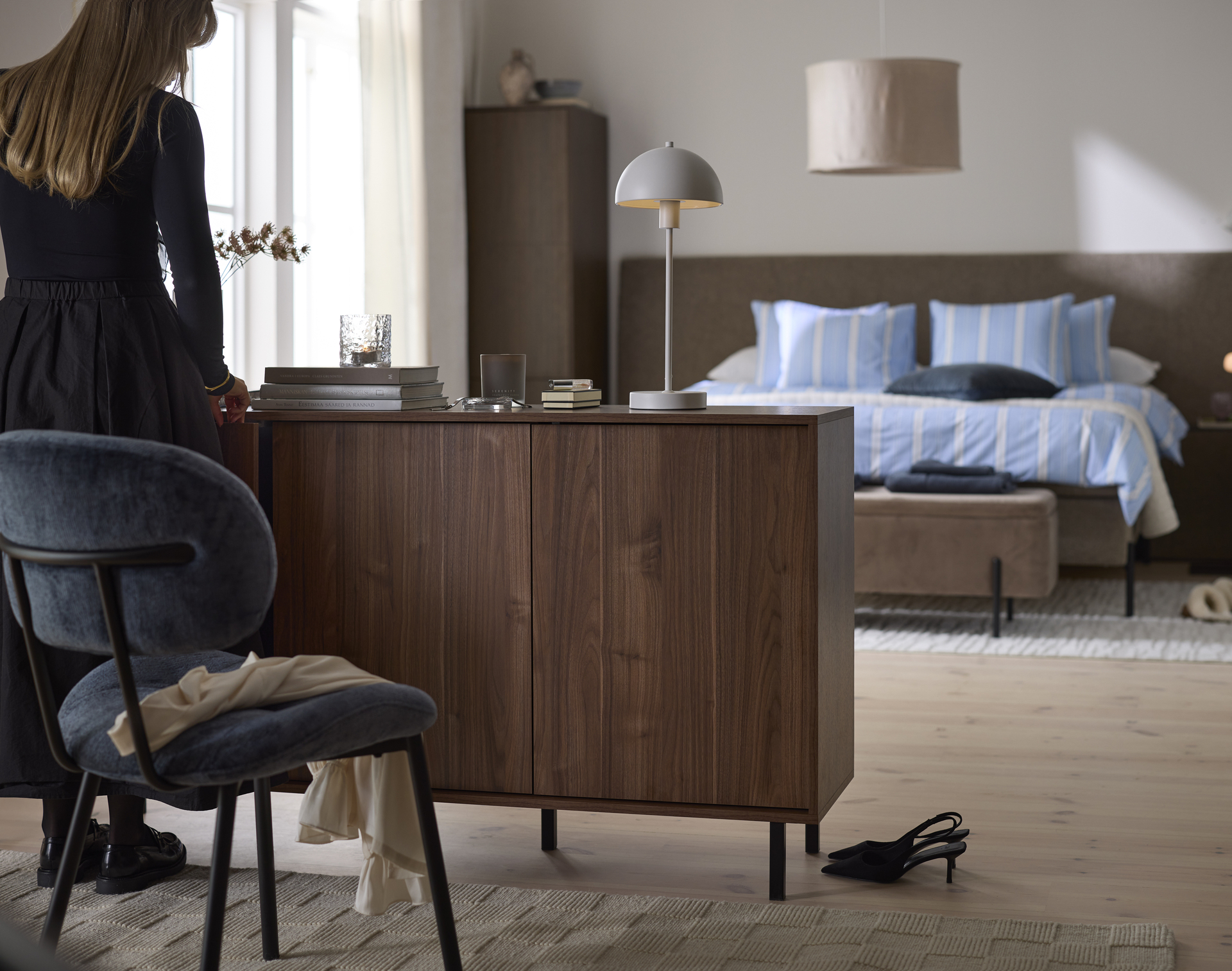 I ett sovrum står en skänk i valnöt. En kvinna öppnar en av luckorna. 