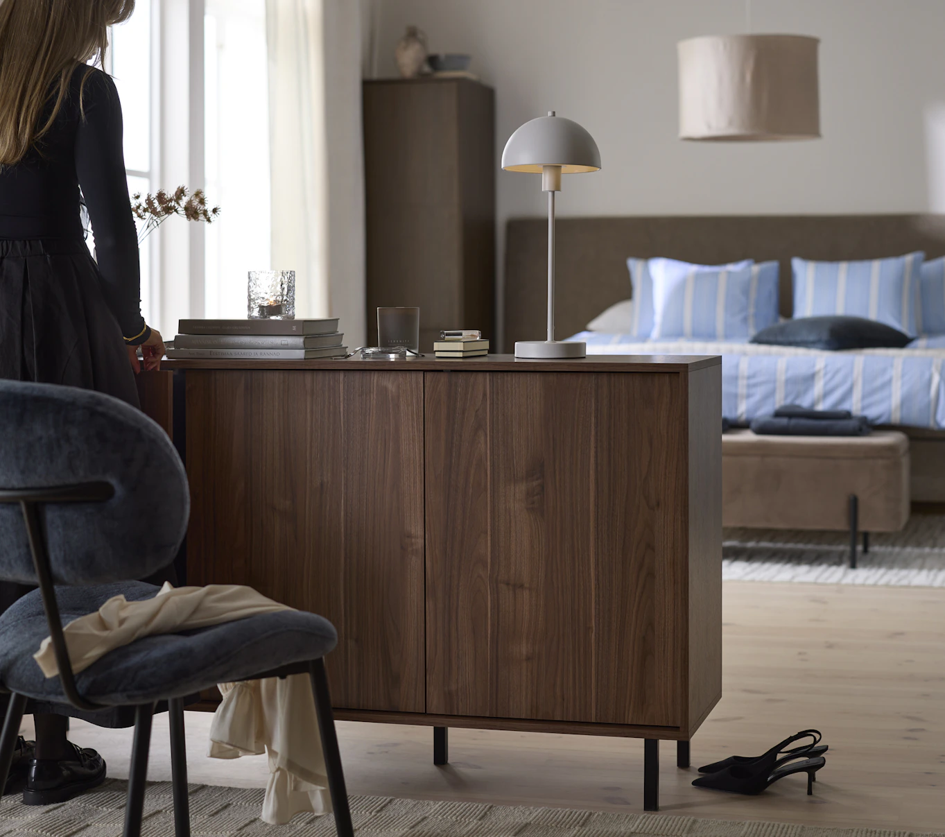 I ett sovrum står en skänk i valnöt. En kvinna öppnar en av luckorna.