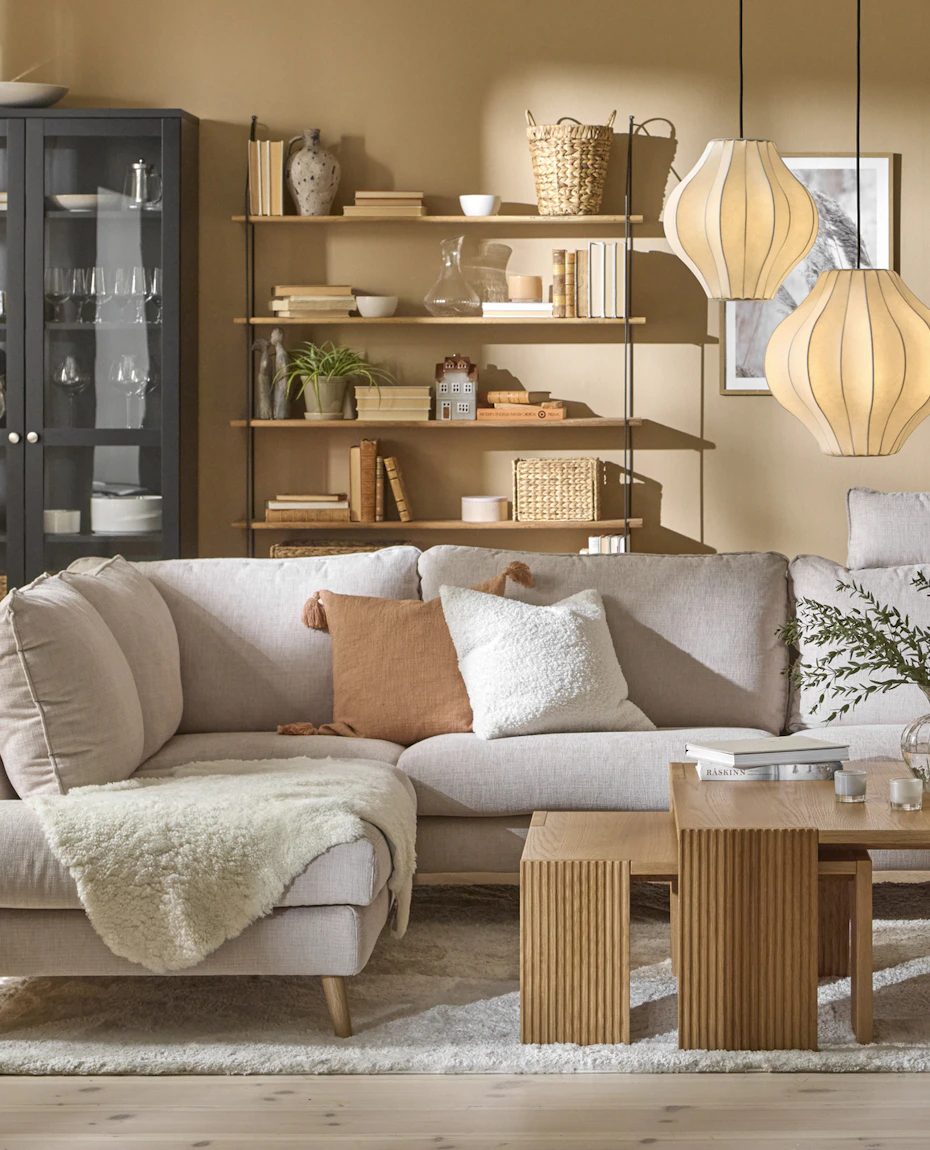 I ett gult vardagsrum står en ljusgrå soffa framför ett svart vitrinskåp och en vägghylla med hyllplan i trä