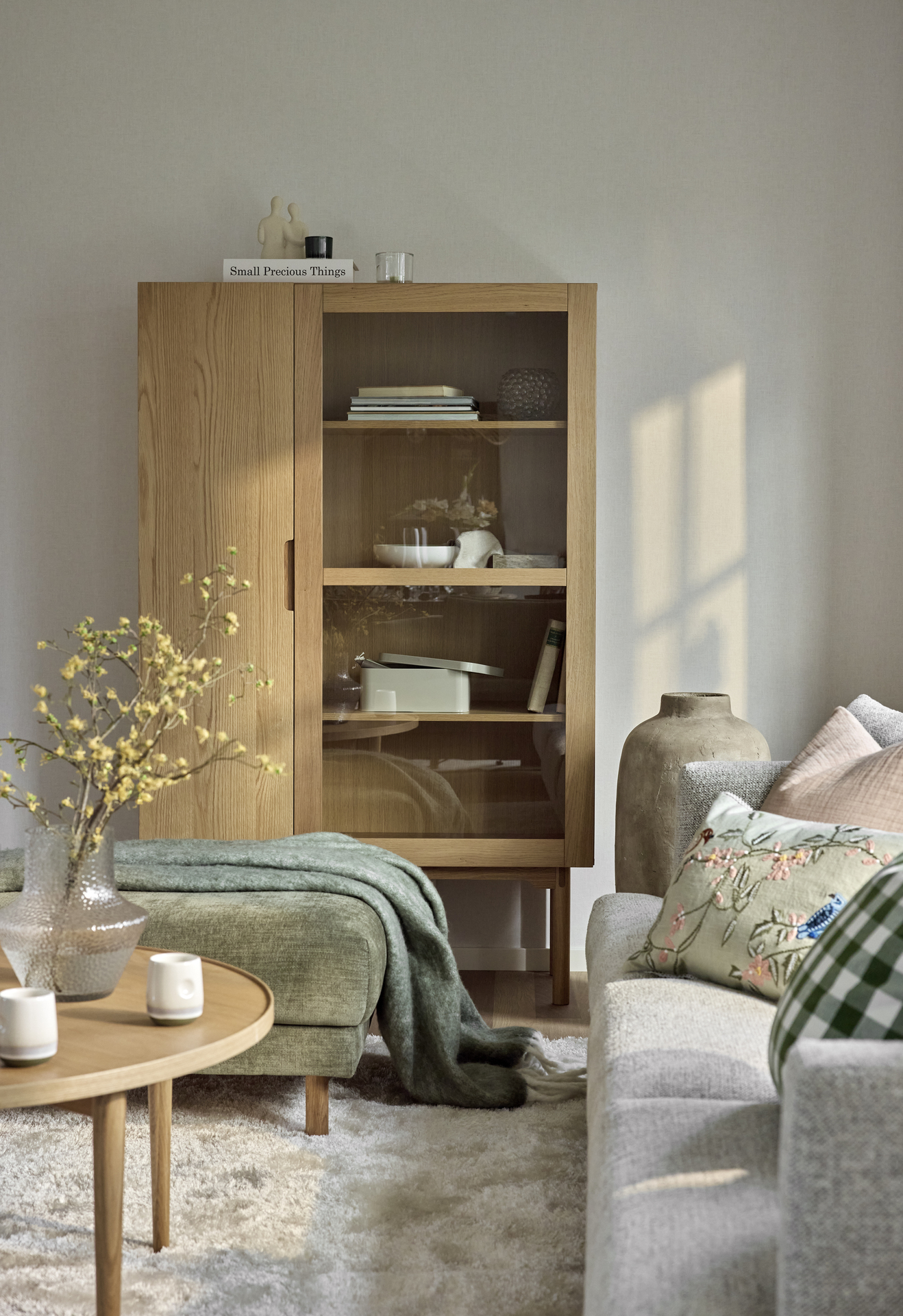 I ett vardagsrum står ett vitrinskåp i ek med prydnadssaker och förvaringslådor