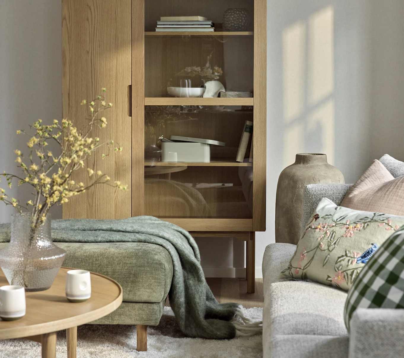 I ett vardagsrum står ett vitrinskåp i ek med prydnadssaker och förvaringslådor