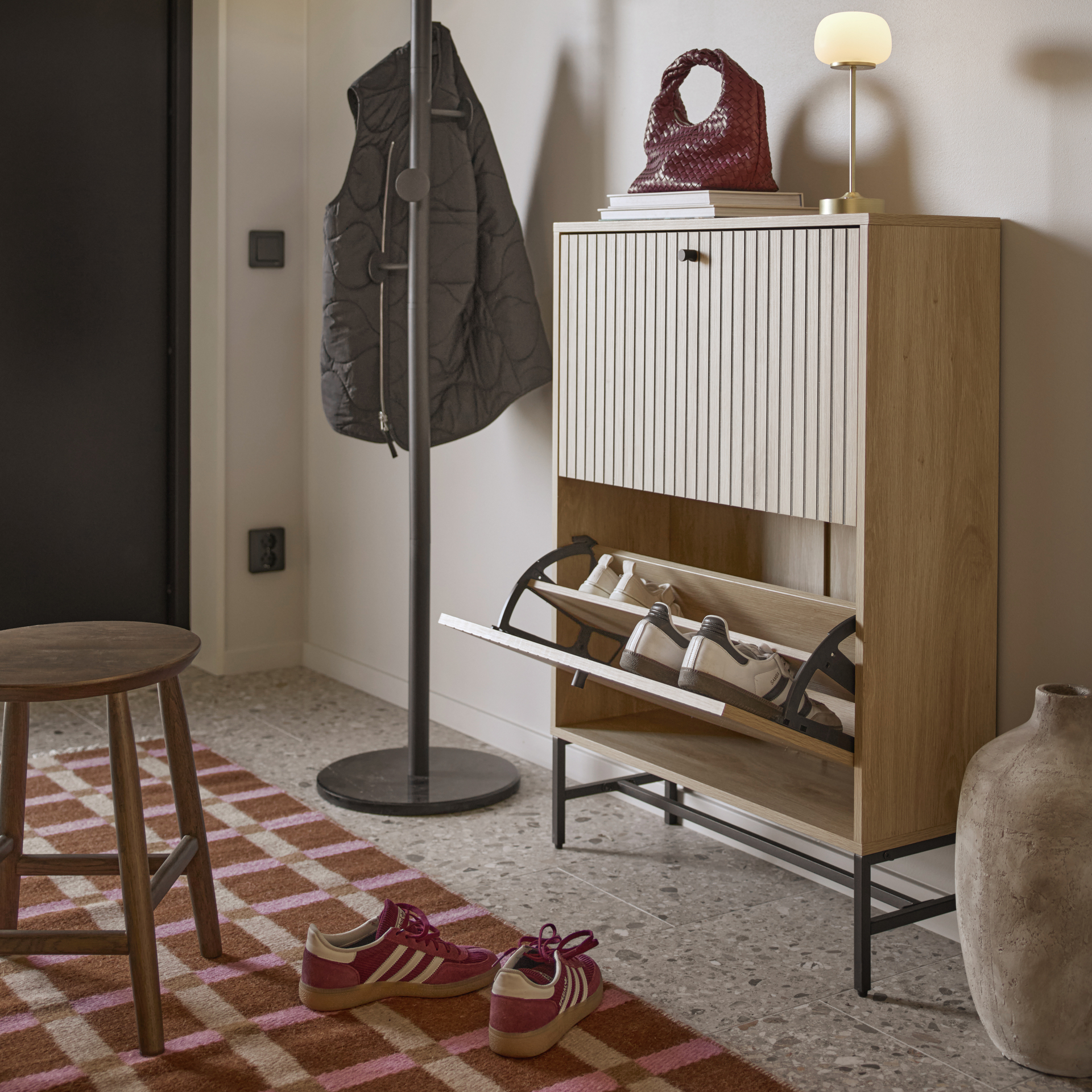 I en hall står ett skoskåp i ribbat ljust trä emot en vägg