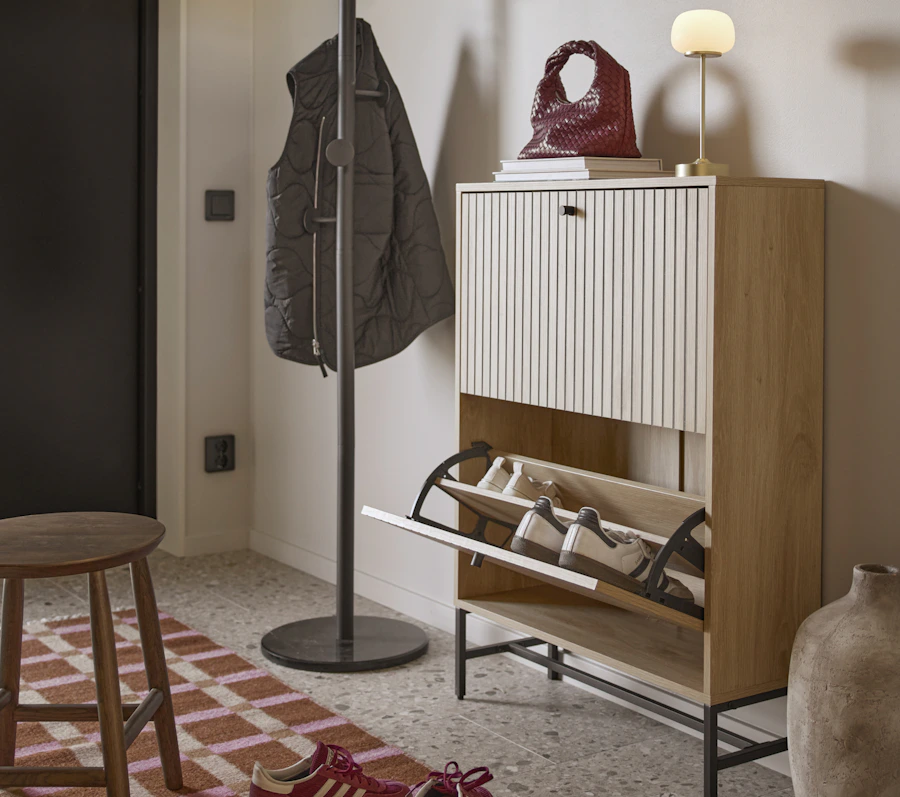 I en hall står ett skoskåp i ribbat ljust trä emot en vägg
