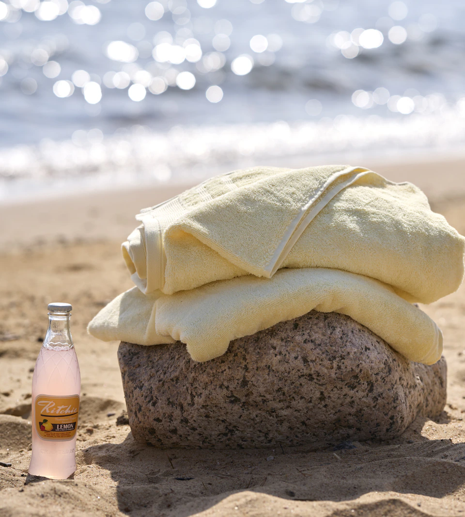 två ihopvikta gula badlakan ligger på en sten på en strand