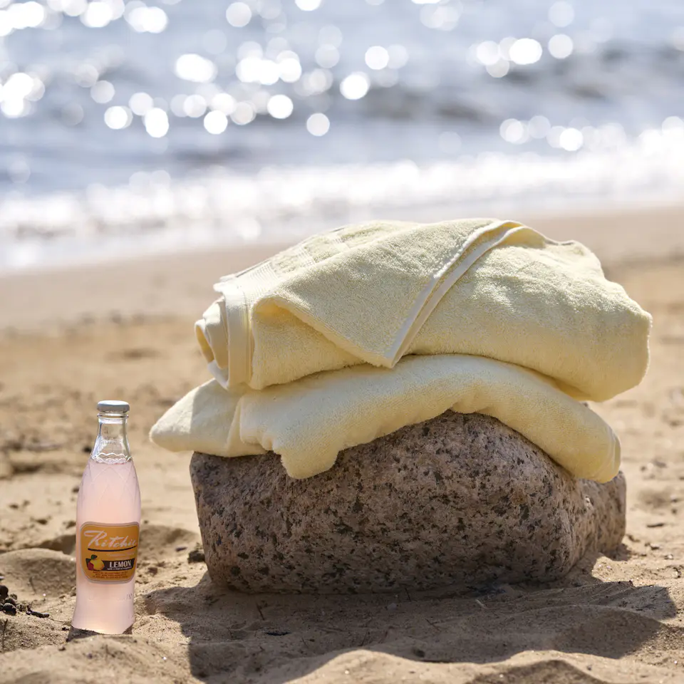 två ihopvikta gula badlakan ligger på en sten på en strand