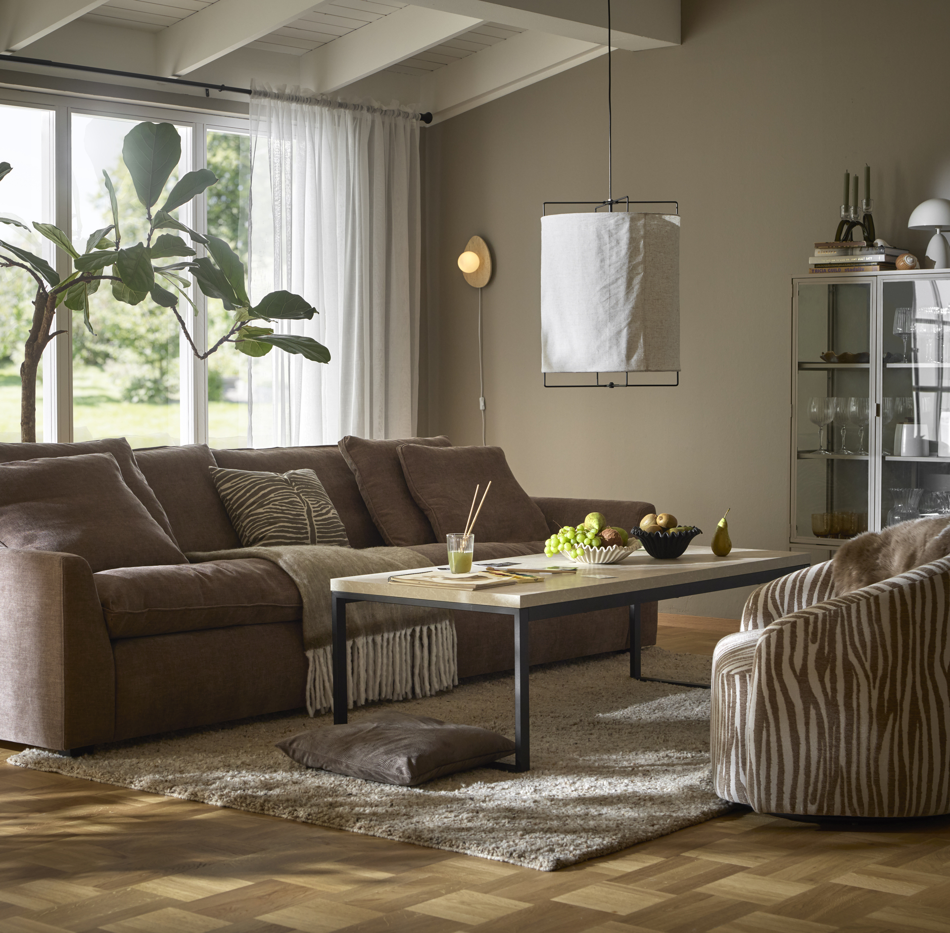 En brun soffa och en fåtölj i beiget zebramönster står i ett beiget vardagsrum.