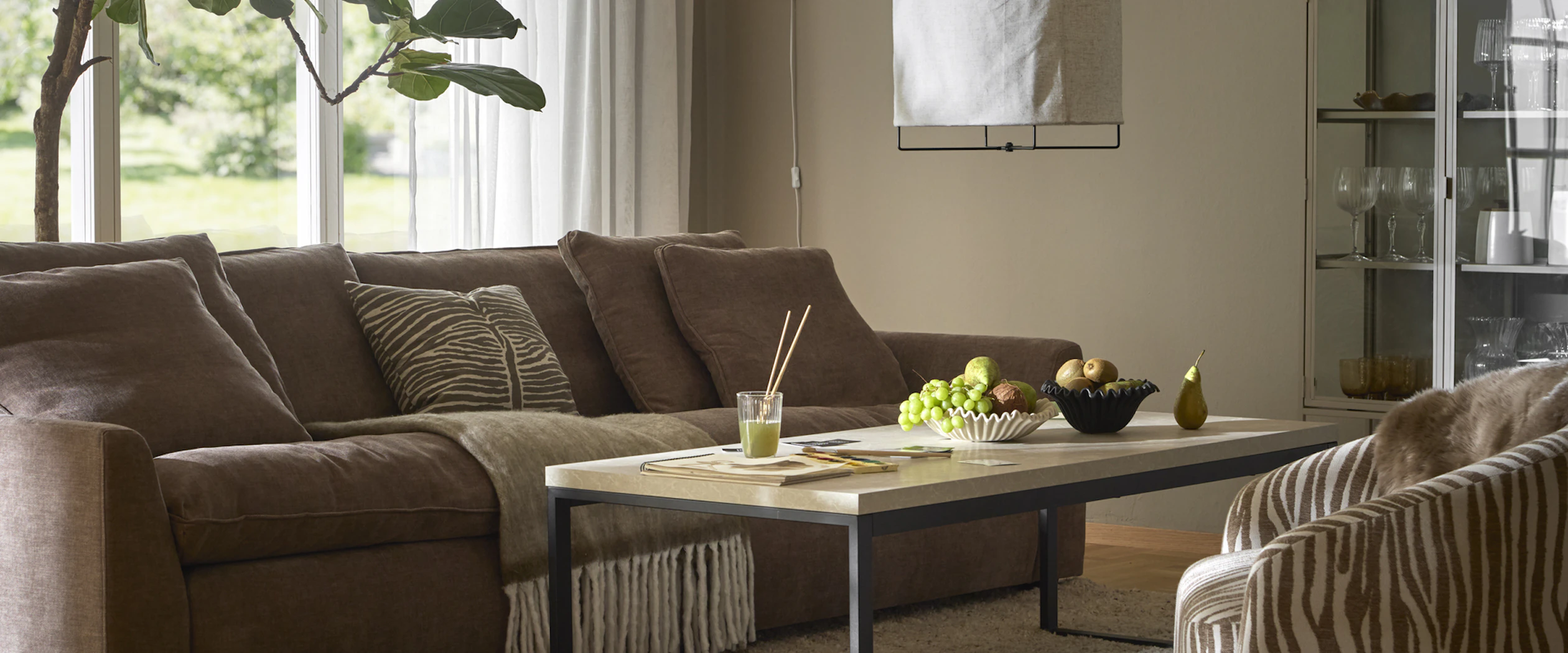 En brun soffa och en fåtölj i beiget zebramönster står i ett beiget vardagsrum.