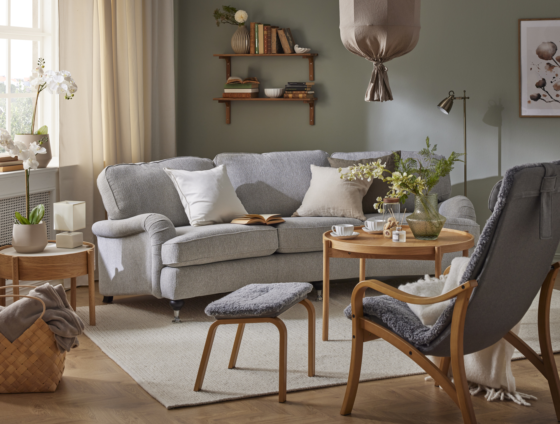 I ett grönt vardagsrum står en grå, svängd Oxford soffa