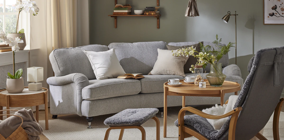 I ett grönt vardagsrum står en grå, svängd Oxford soffa