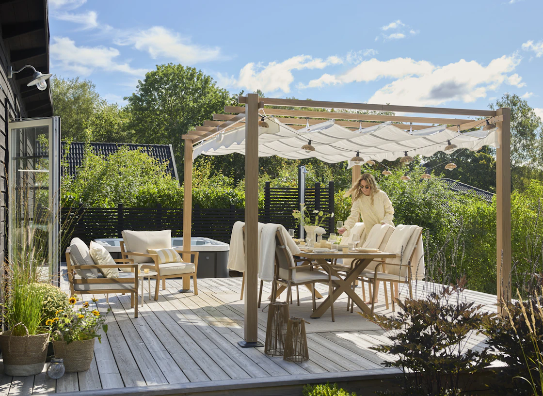 Uteplats med utematgrup under en stor pergola en solig sommardag i en modern villaträdgård.
