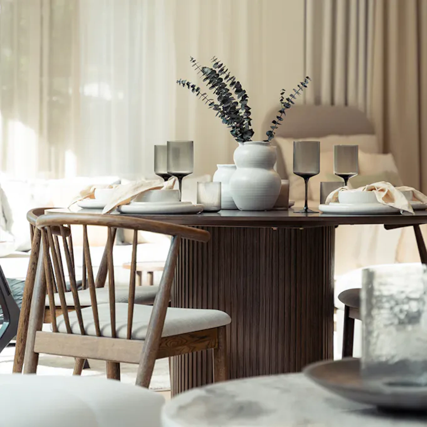 Ljust matplatsrum med närbild på matbord med stor ribbad bas i mörkt trä och trästolar i mörkt trä intill. 